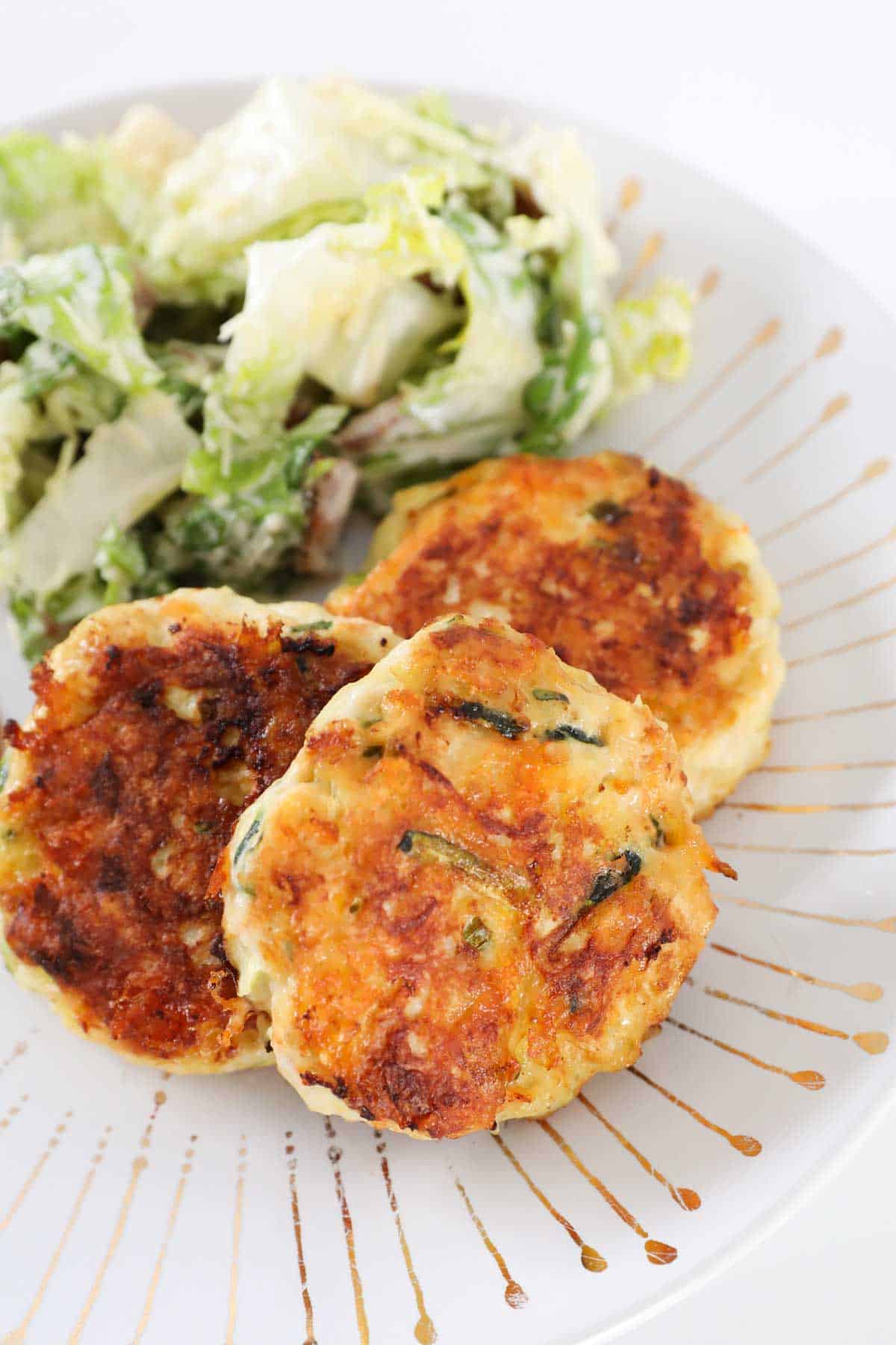 Three chicken rissoles on a plate with salad.