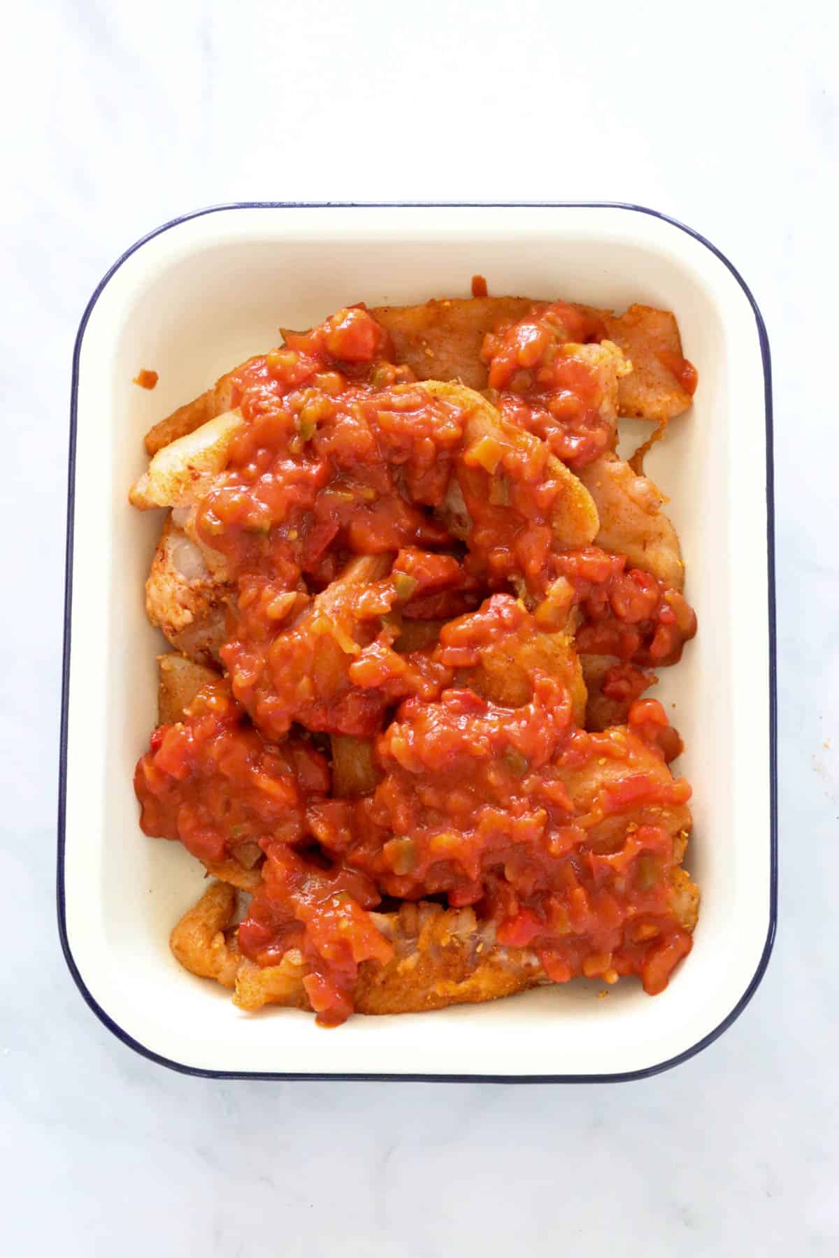 Salsa on top of spicy chicken pieces in a baking dish.