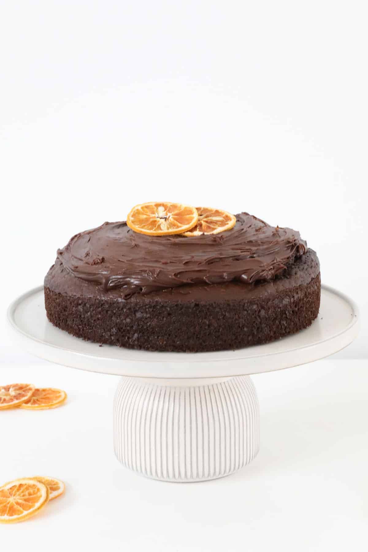 Chocolate orange cake, decorated with slices of dried orange, served on a white cake stand.