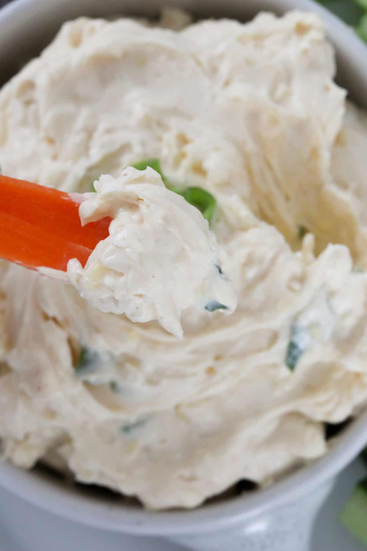 Close up image of a carrot dipping into a cream cheese dip.