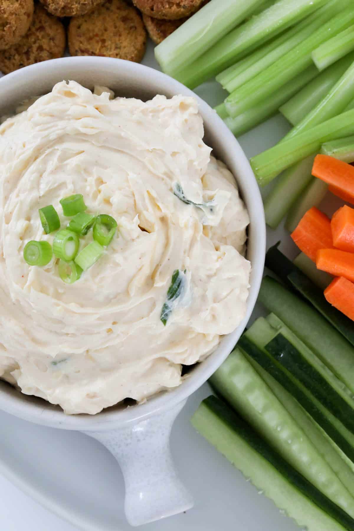 Carrot, cucmber and celery sticks placed around a small white bowl of dip.