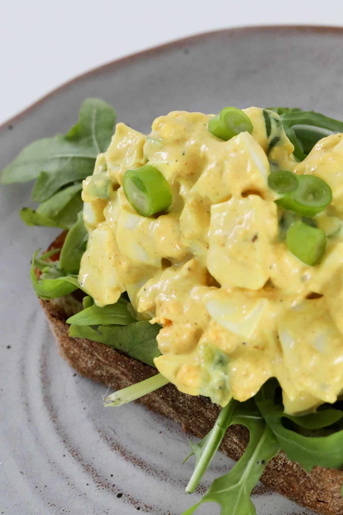 A close up of egg salad on lettuce and rye bread.