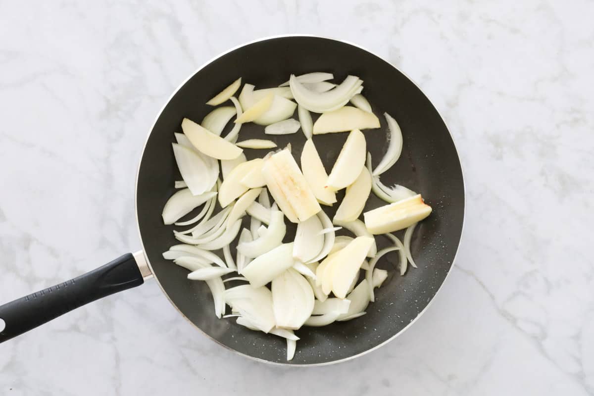 Wedges of apple and onion in a frying pan.