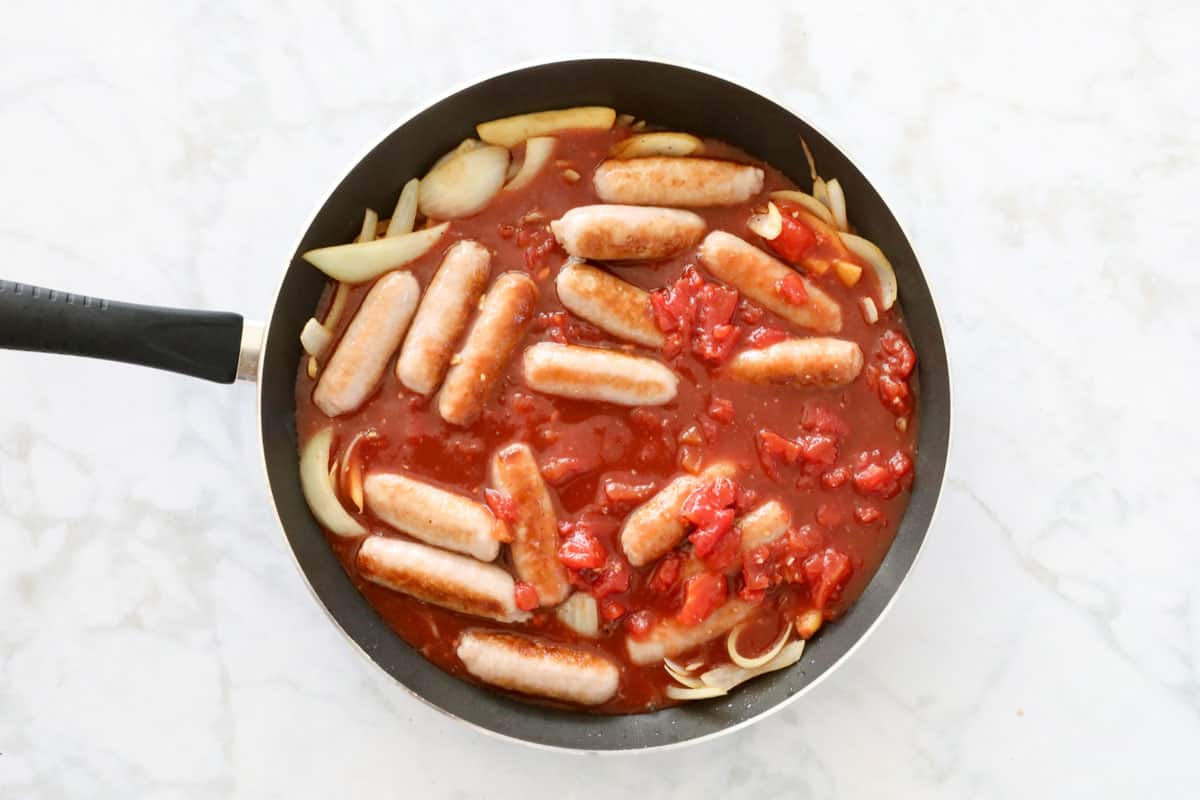 Sausages and sauce ingredients in a pan.