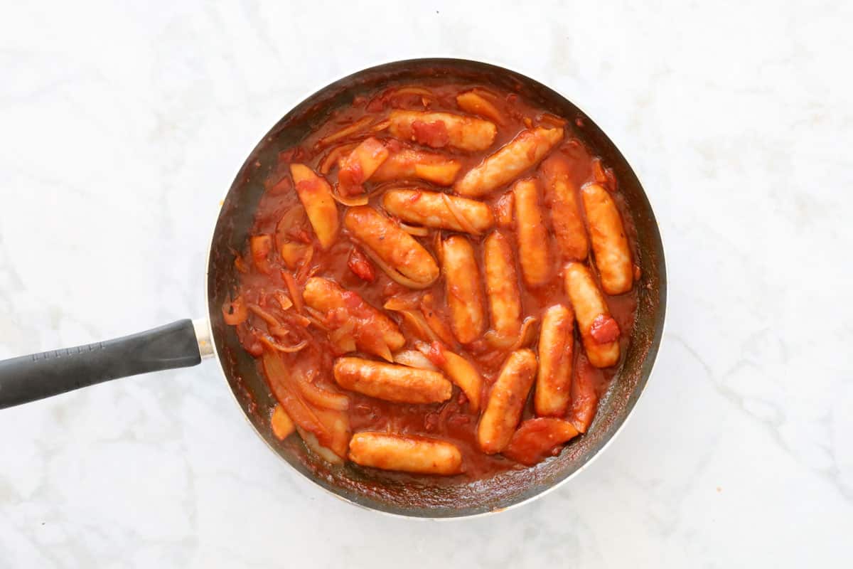 Devilled sausages in a pan with tomato sauce.