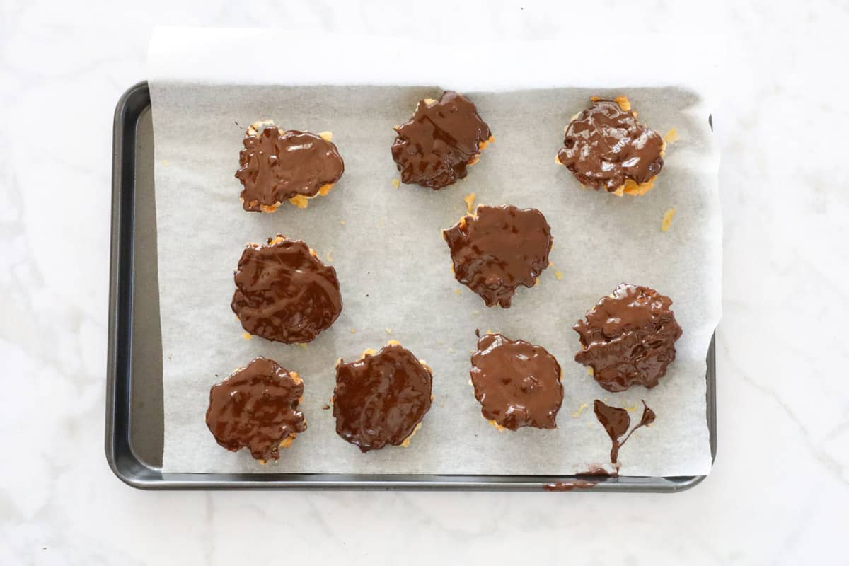 Florentines coated with melted dark chocolate on a baking tray.