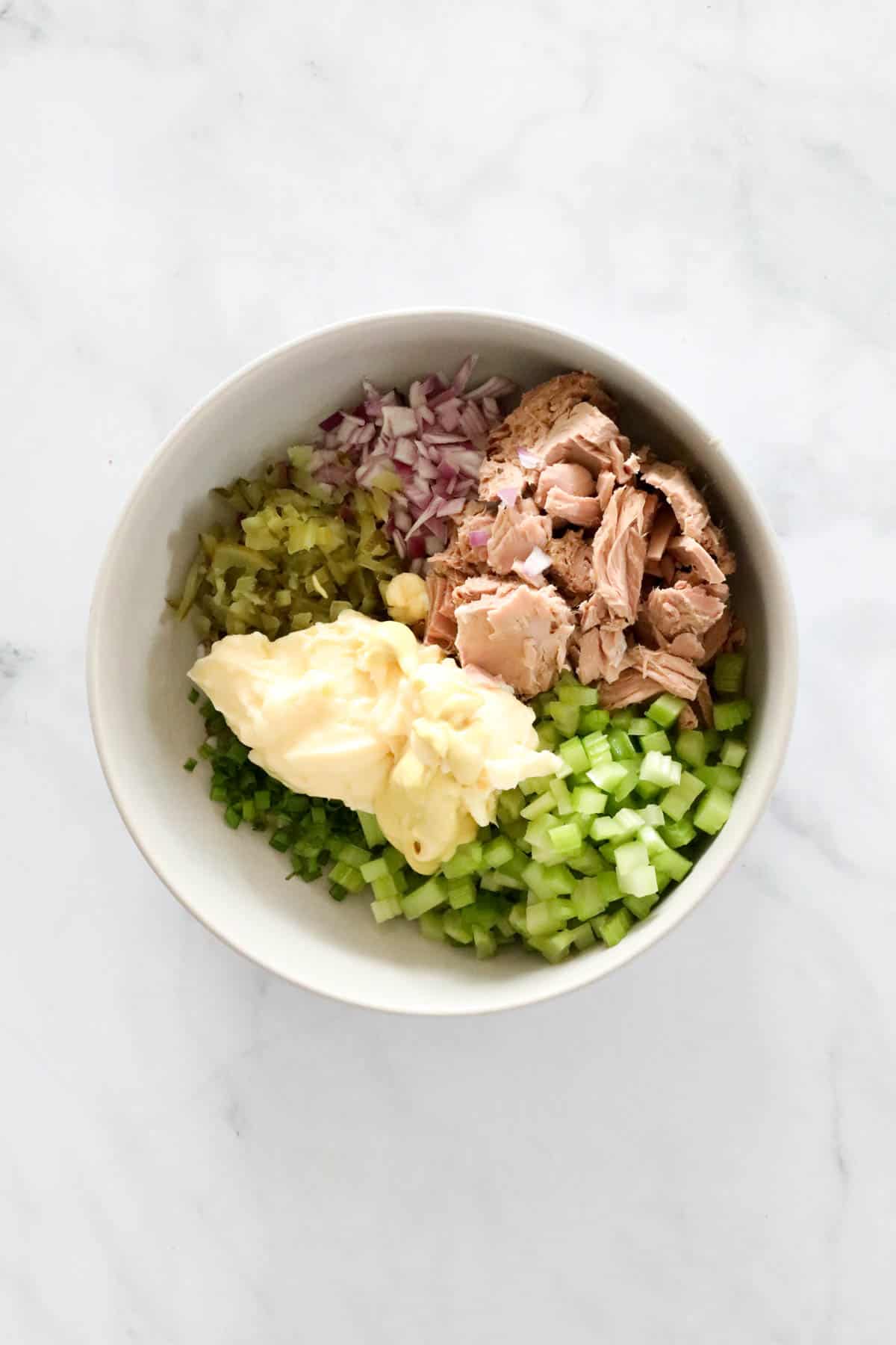 The ingredients for tuna salad in a mixing bowl with a dollop of mayo on top.
