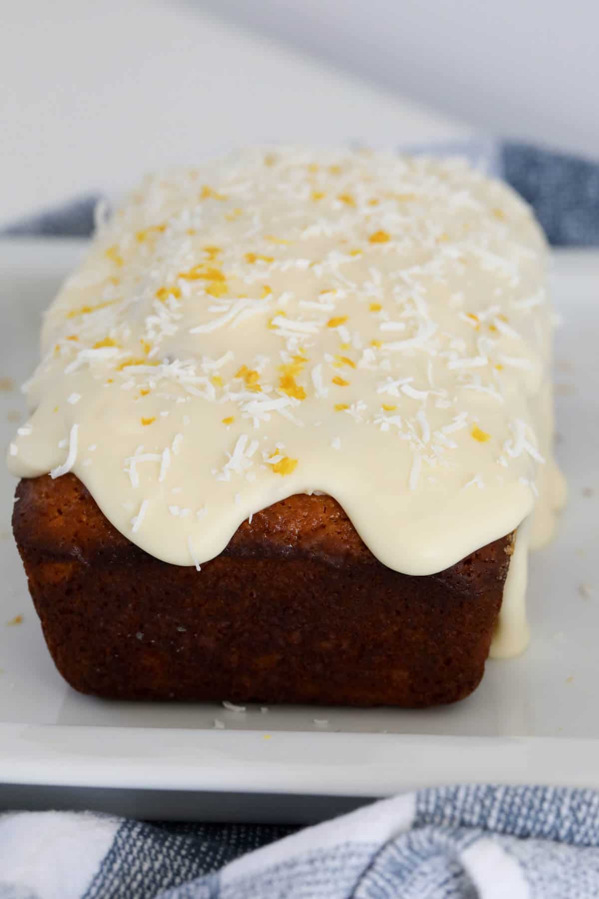 A lemon loaf covered in cream cheese frosting and sprinkled with coconut and lemon zest.