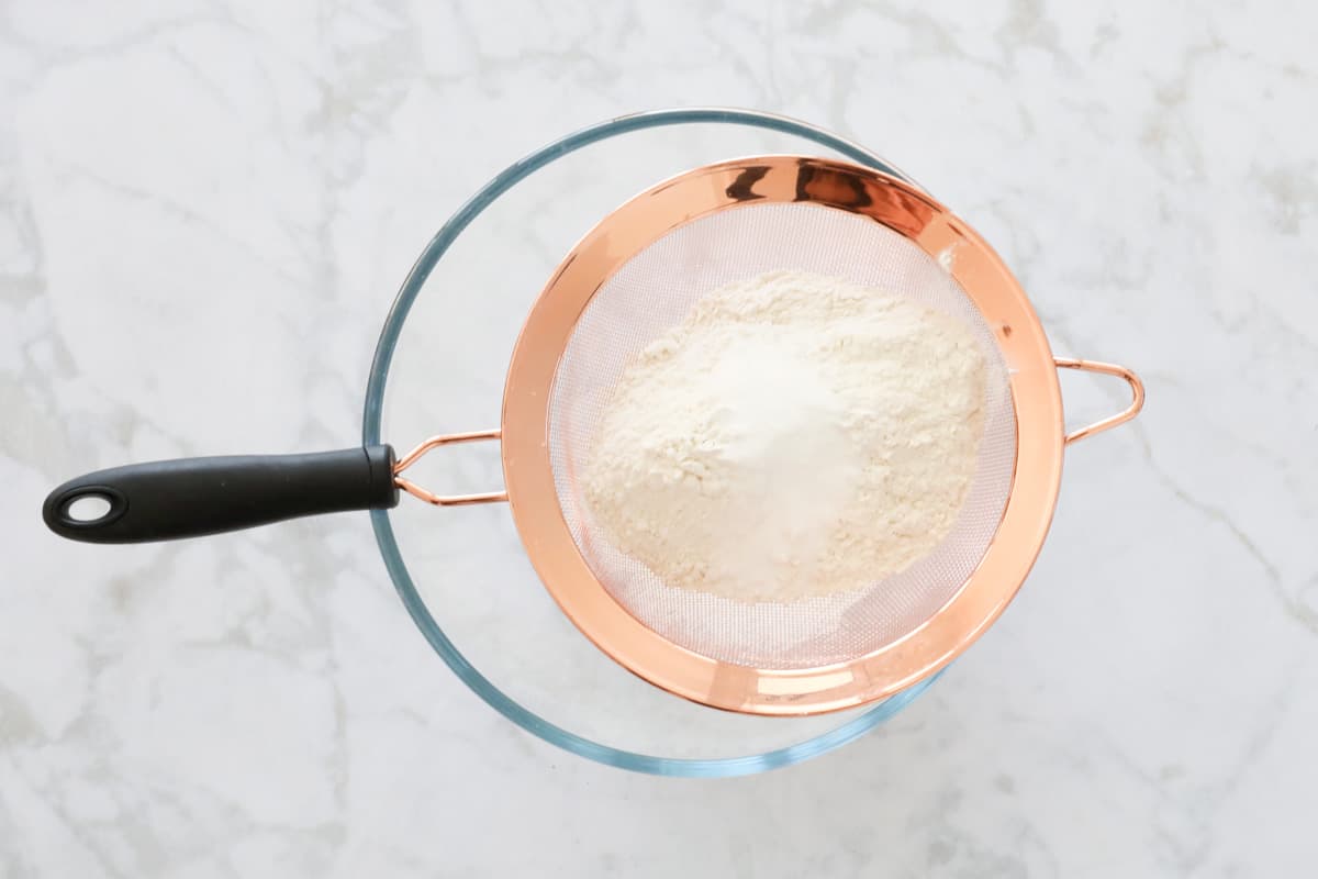 Sifting flour into a glass mixing bowl with a copper sifter.