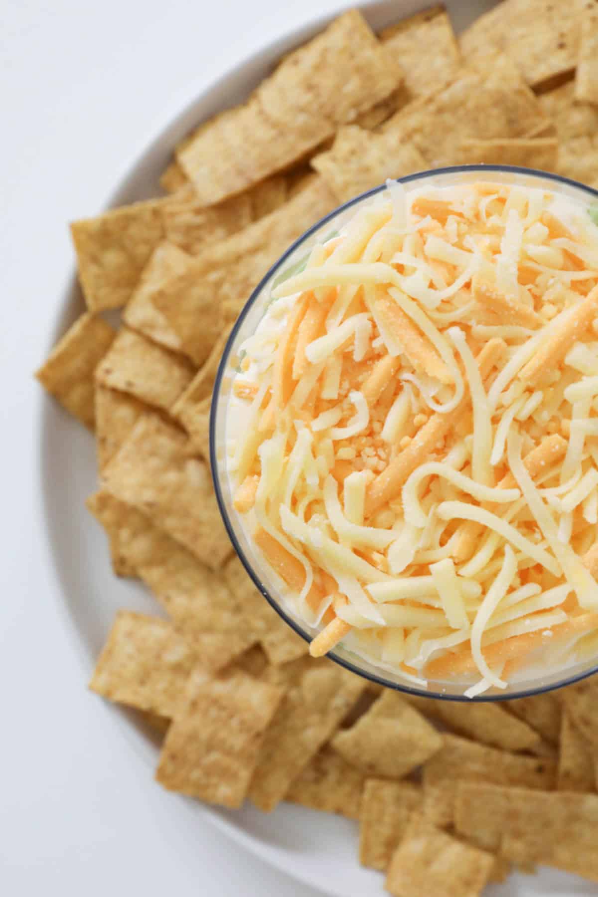 A plate of tortilla strips surrounding a bowl of mexican layer dip topped with grated cheese.