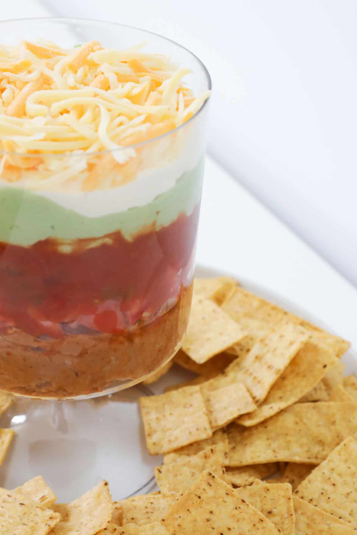 A side shot of layered mexican dip with corn chips underneath.