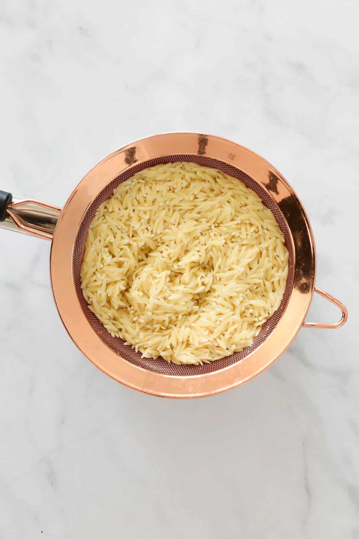 Cooked risoni pasta in a copper sieve.