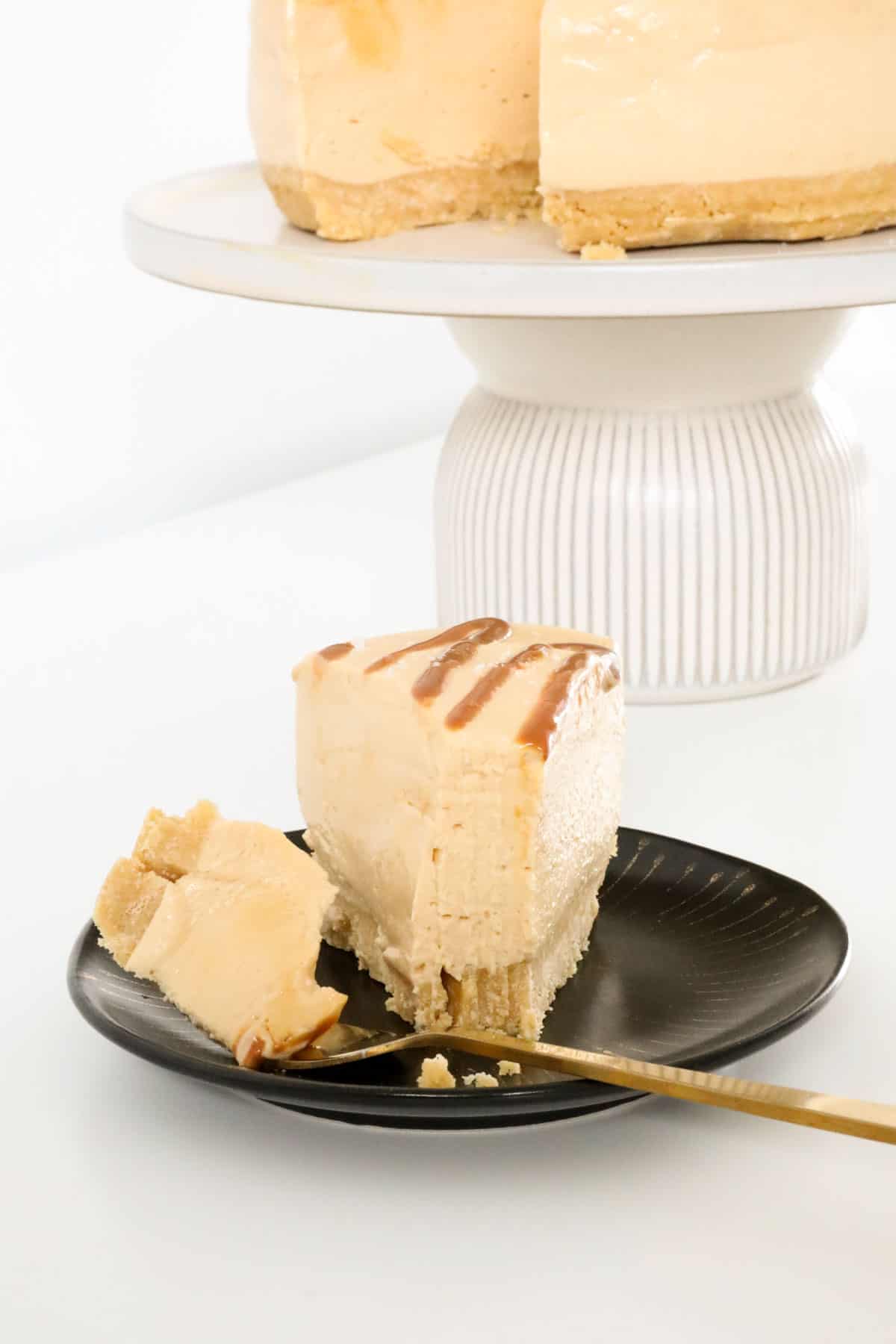 A piece of cheesecake on a black plate with a gold fork.