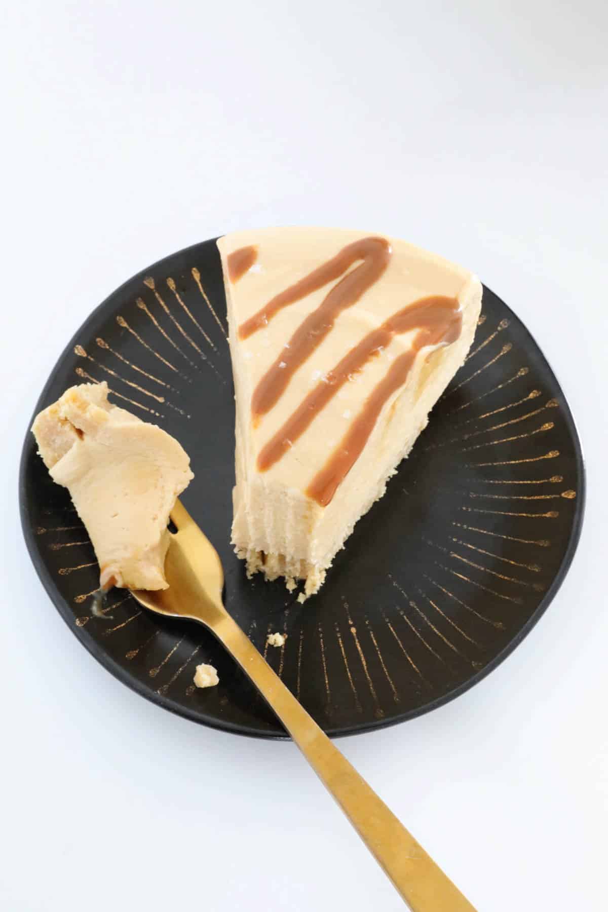 An overhead shot of a slice of dessert drizzled with caramel sauce, served on a black plate.
