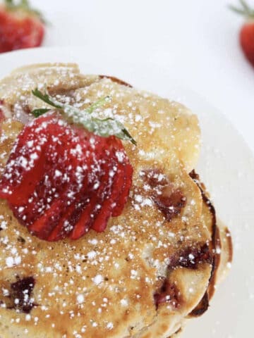 An overhead shot of a plate of strawberry pancakes with icing sugar on top.