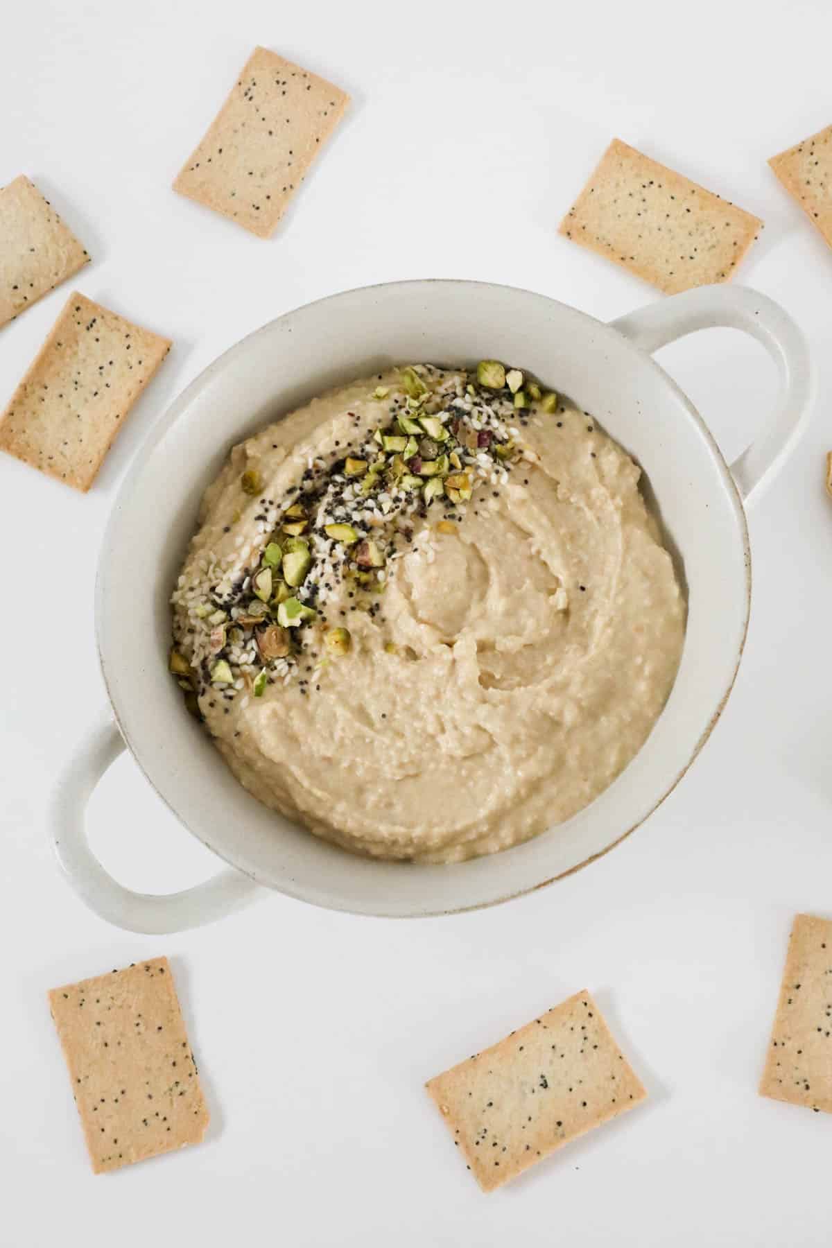 An overhead shot of a bowl of hummus with dukkah, and lavosh crackers.