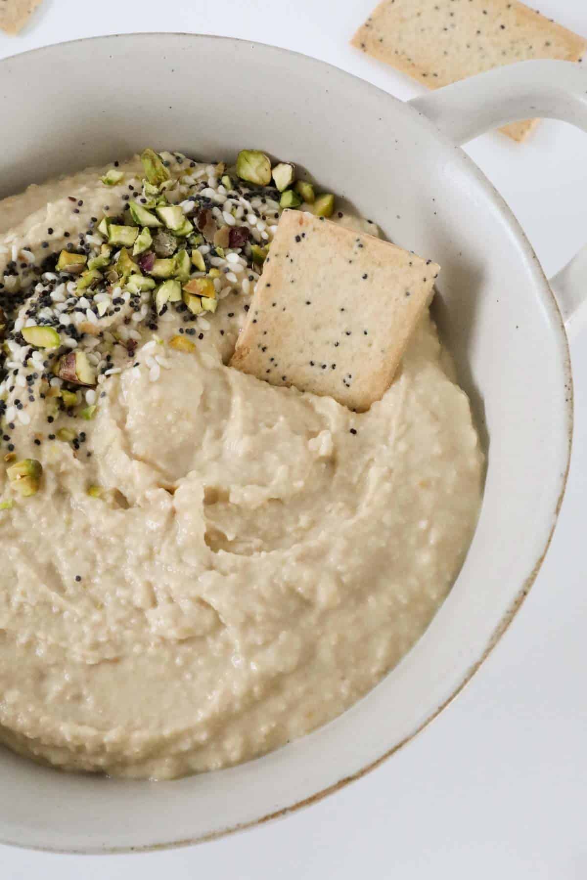 A lavosh cracker dipped in to a bowl of hummus.