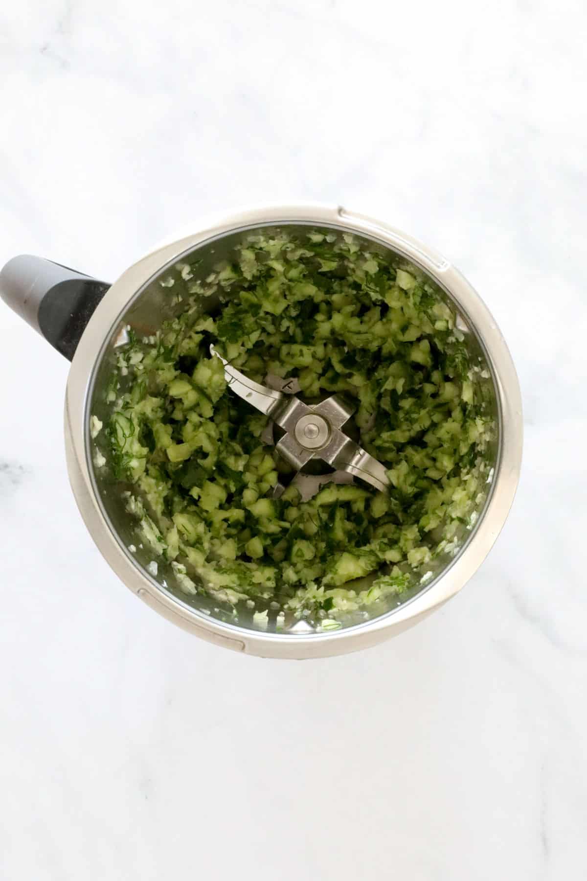Chopped cucumber, garlic, mint and dill in a Thermomix.