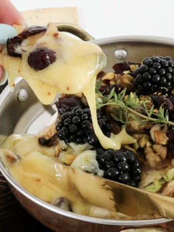Oozy warm cheese in a dish filled with nuts and blackberries.