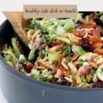 Two wooden serving spoons in a bowl of crunchy broccoli, bacon, almond and cranberry salad.