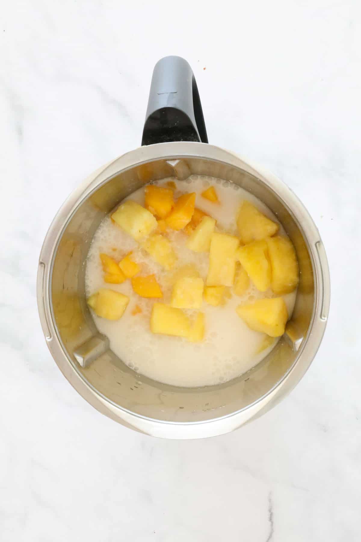 Chunks of mango, pineapple and coconut milk in a stainless jug.