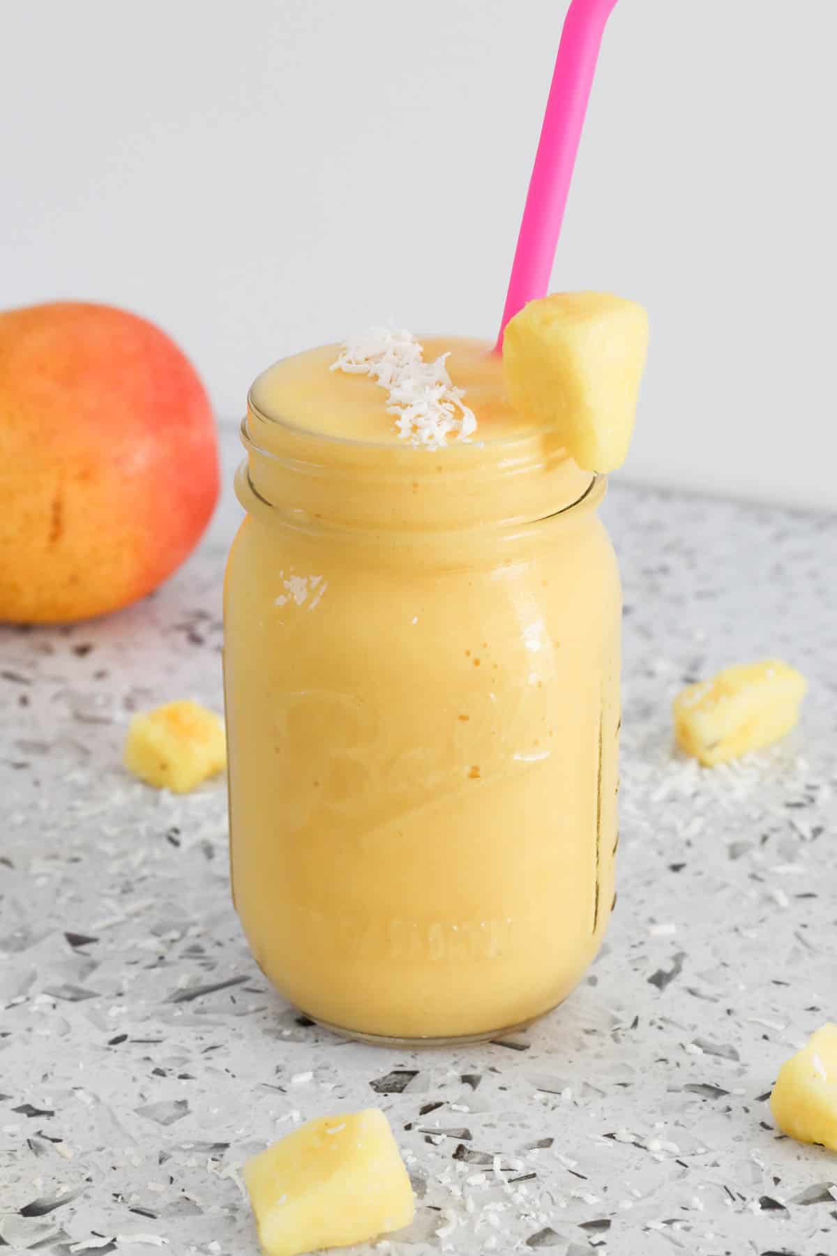 Mango pineapple smoothie in a glass jar with a pink straw.