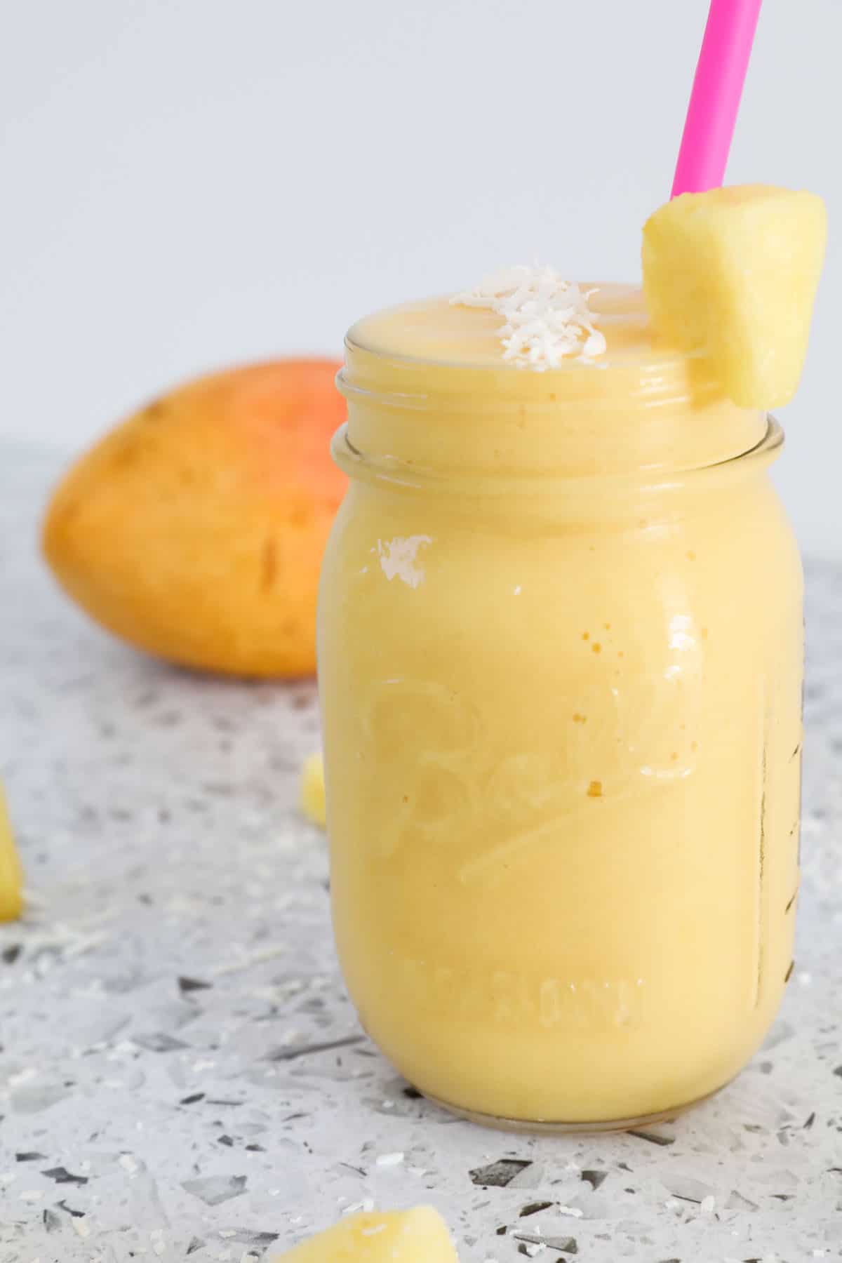 A smoothie in a glass jar with a mango in the background.