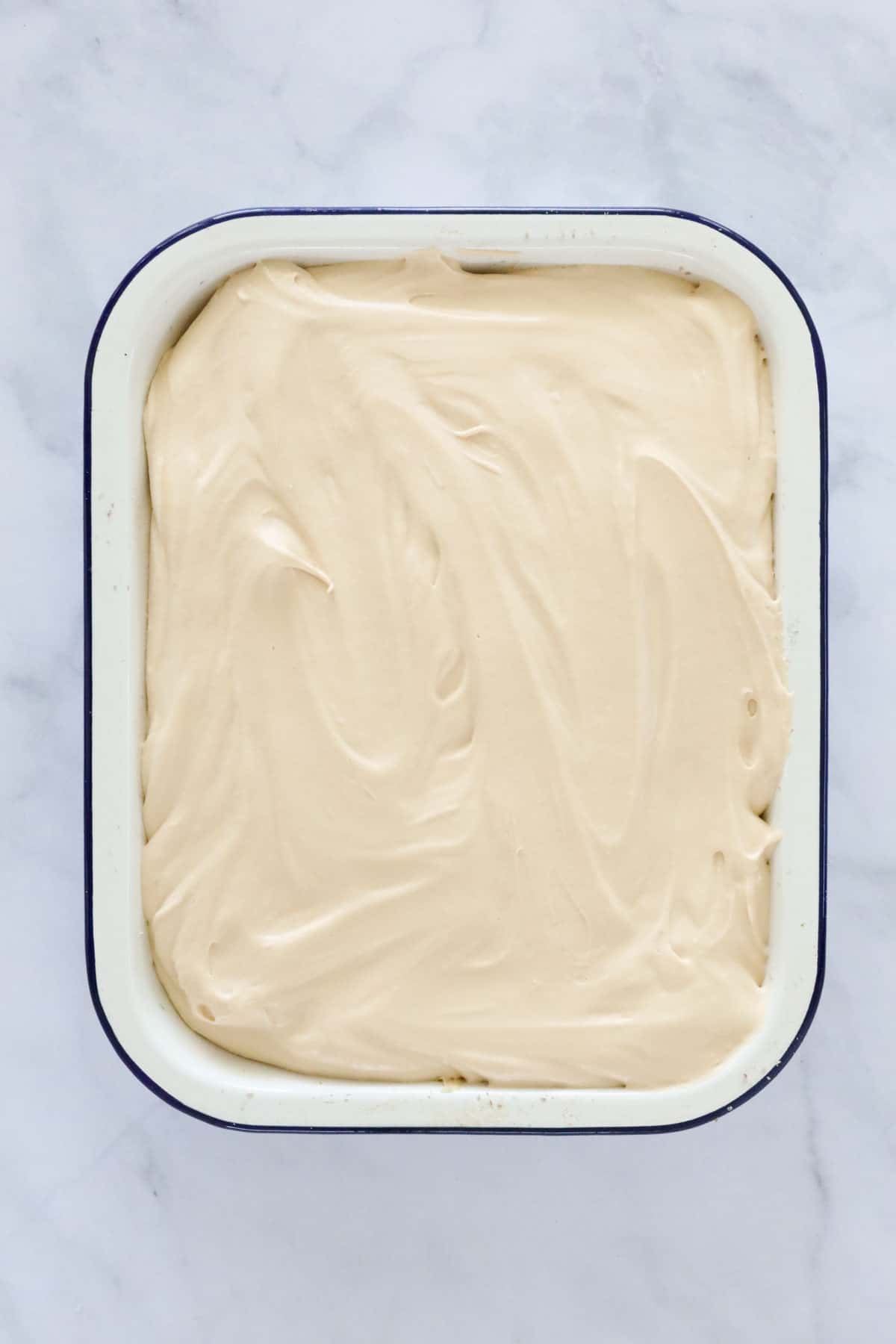 Caramel cream spread over biscuits in a baking tin.
