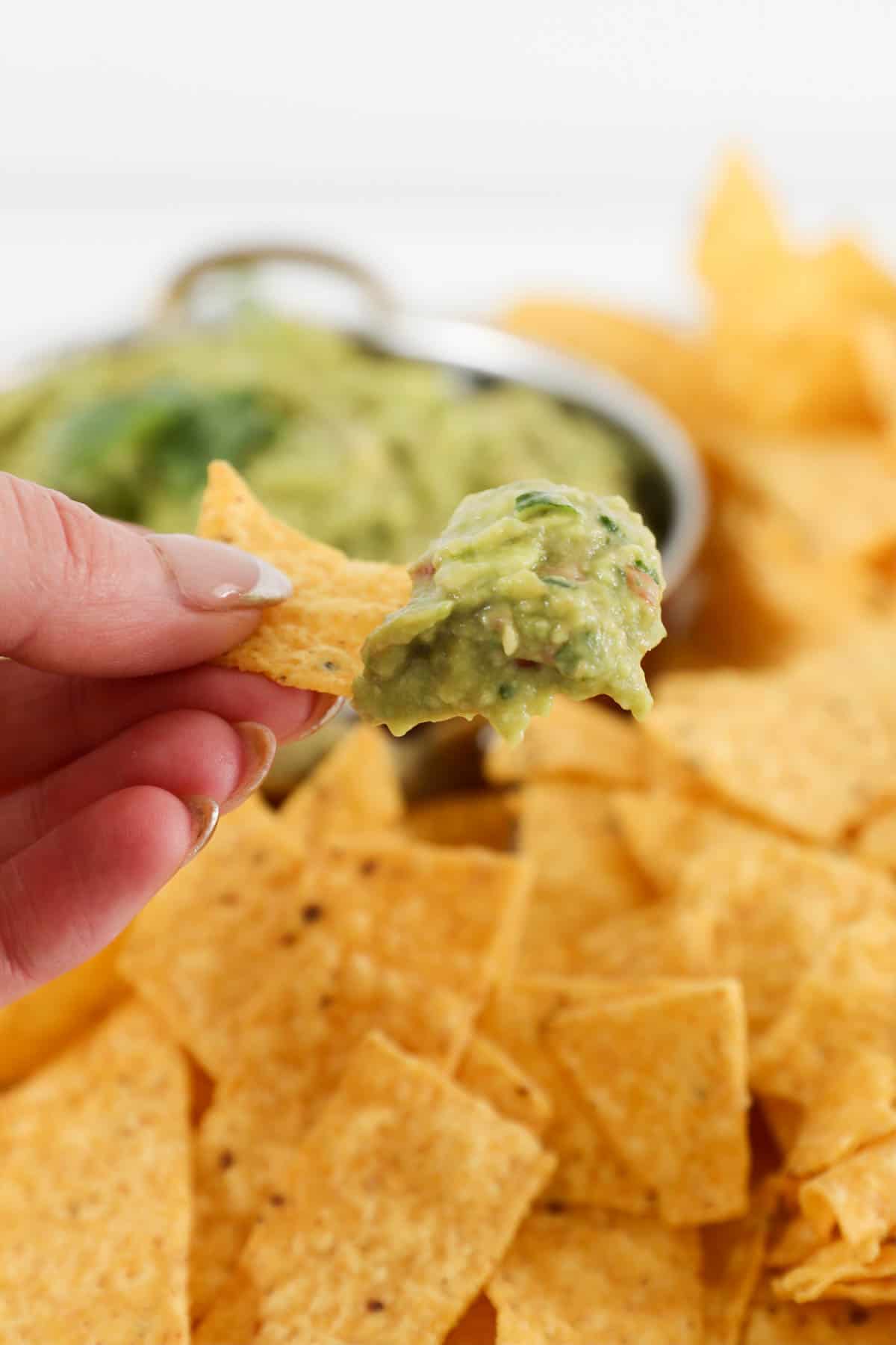 A hand holding a tortilla chip with guacamole.