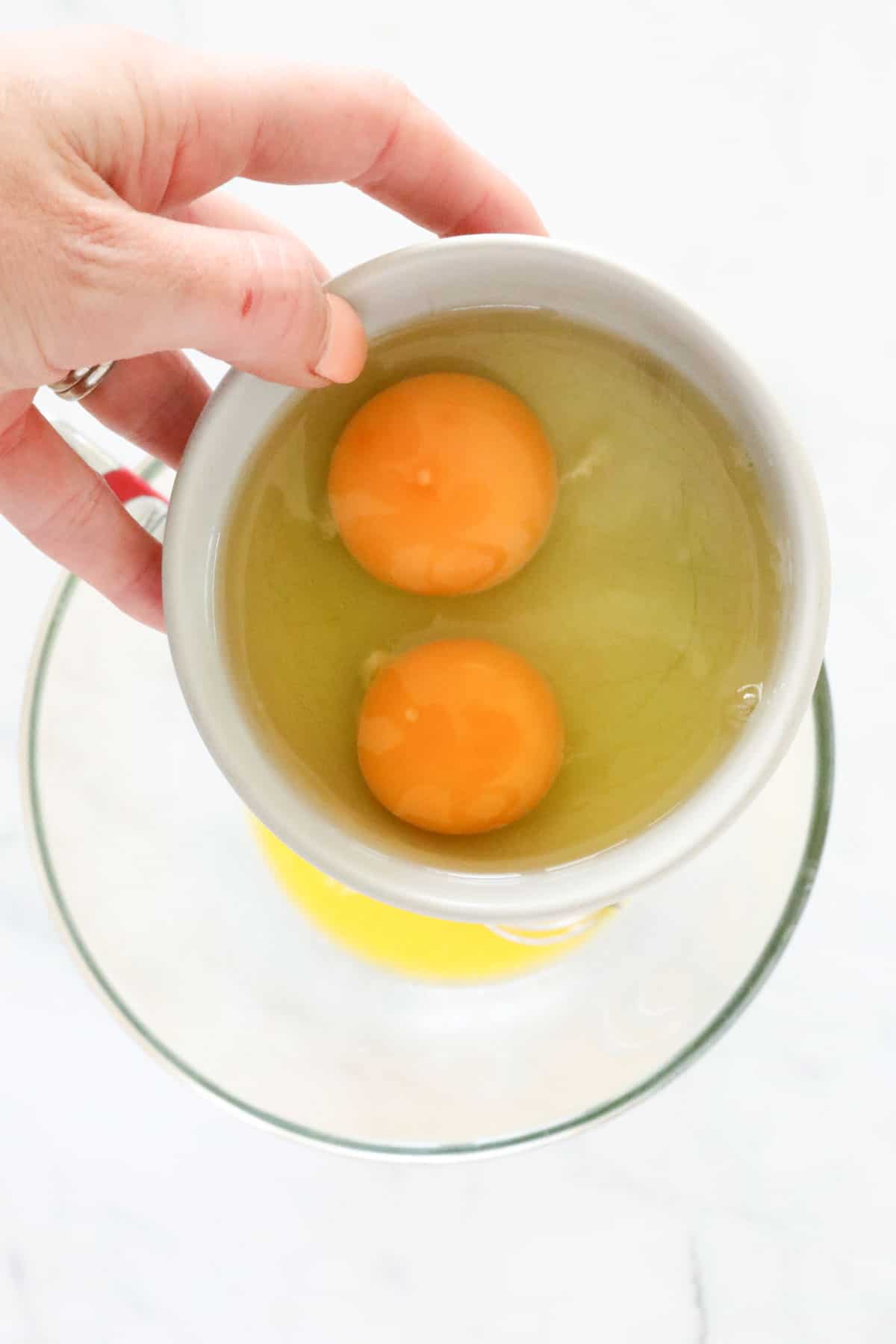 A hand holding a bowl with two eggs in it. 