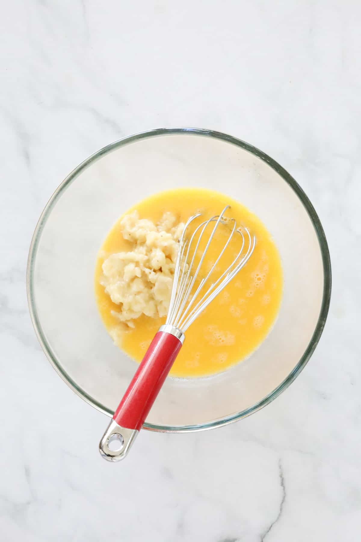 Mashed banana added to wet ingredients in a bowl with a whisk.