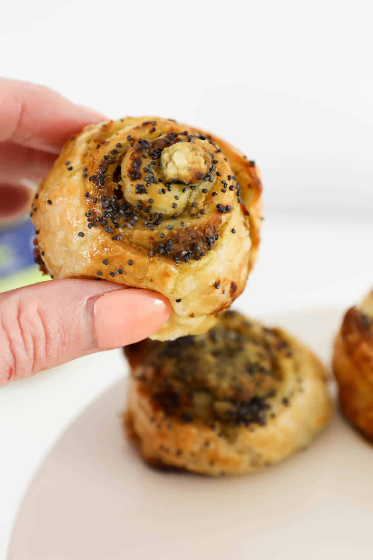 A hand holding up a golden baked pastry sprinkled with poppy seeds.