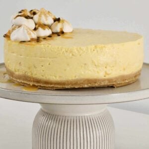 A mango cheesecake on a cake stand with meringue and passionfruit on top.