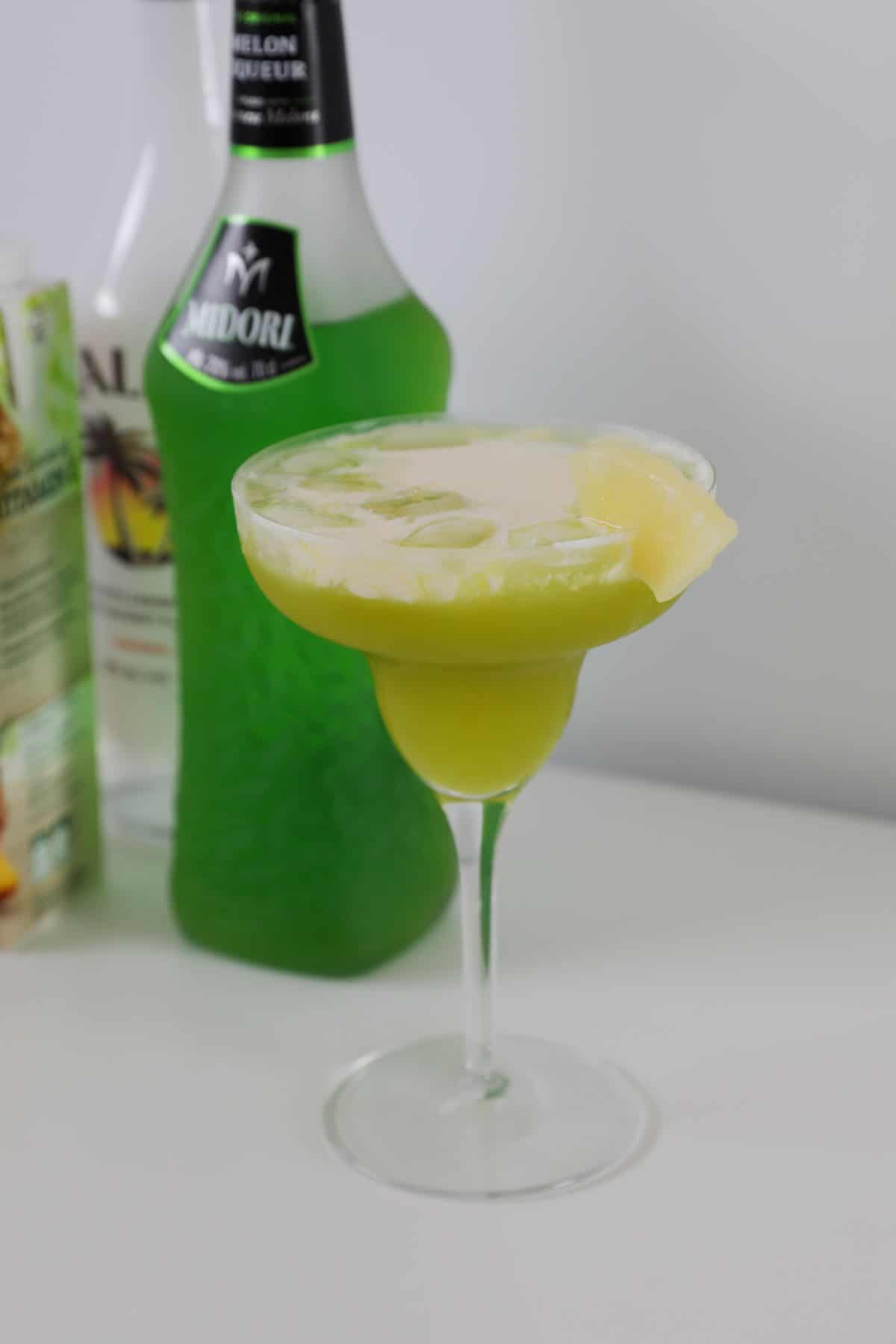 A midori splicein a cocktail glass with pineapple garnish.