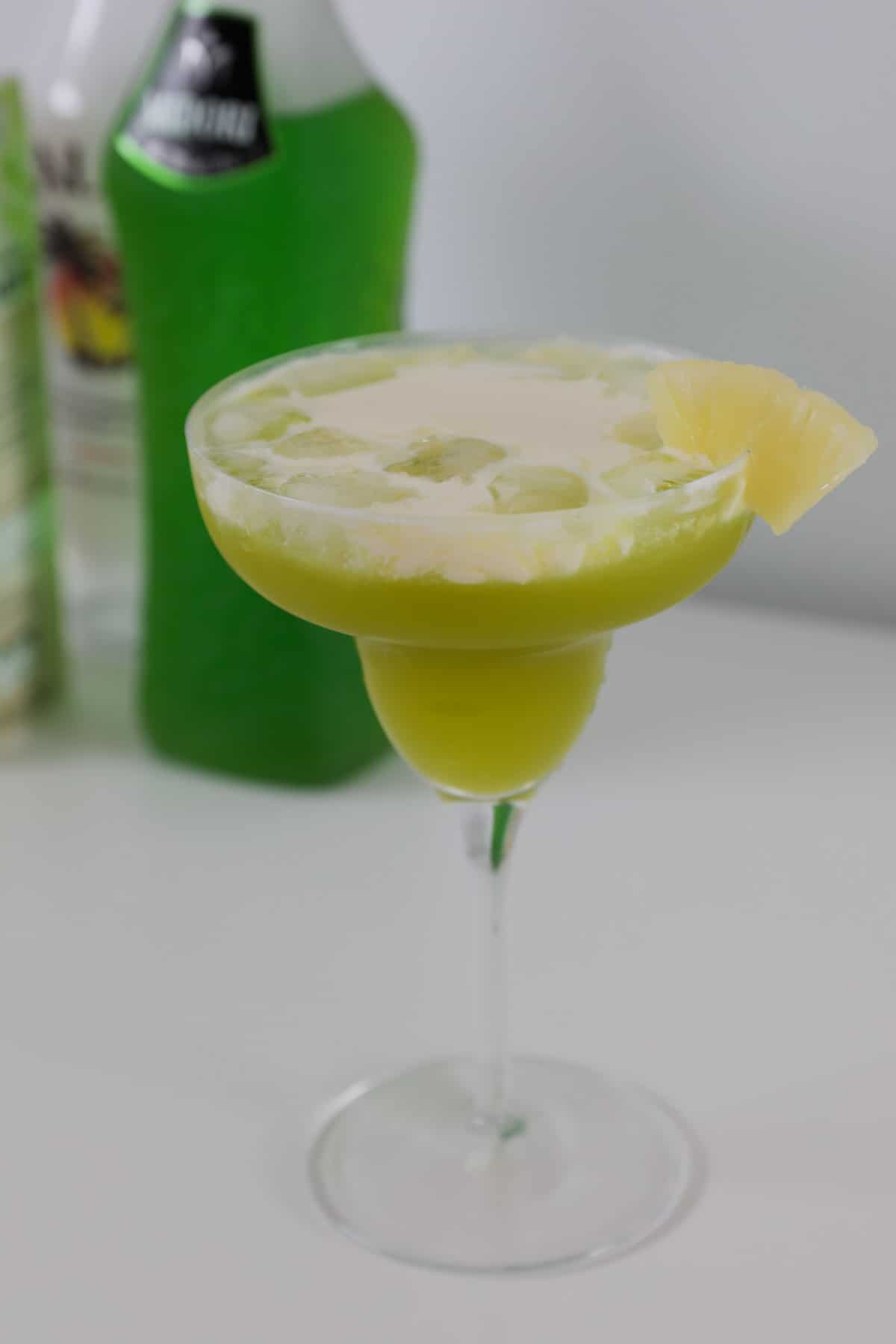 A green cocktail topped with cream in front of a bottle of Midori.