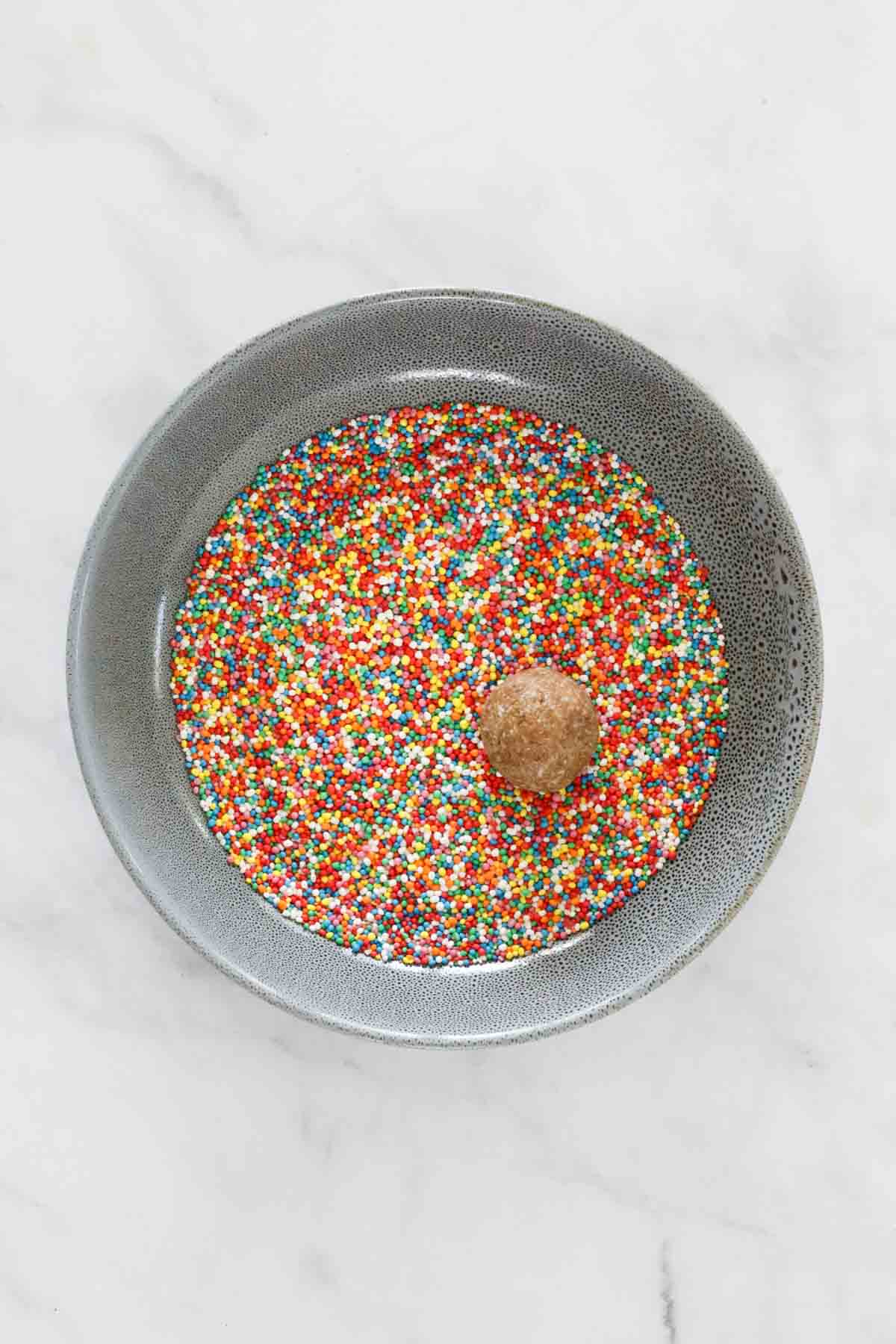 A round ball in a plate of coloured sprinkles.