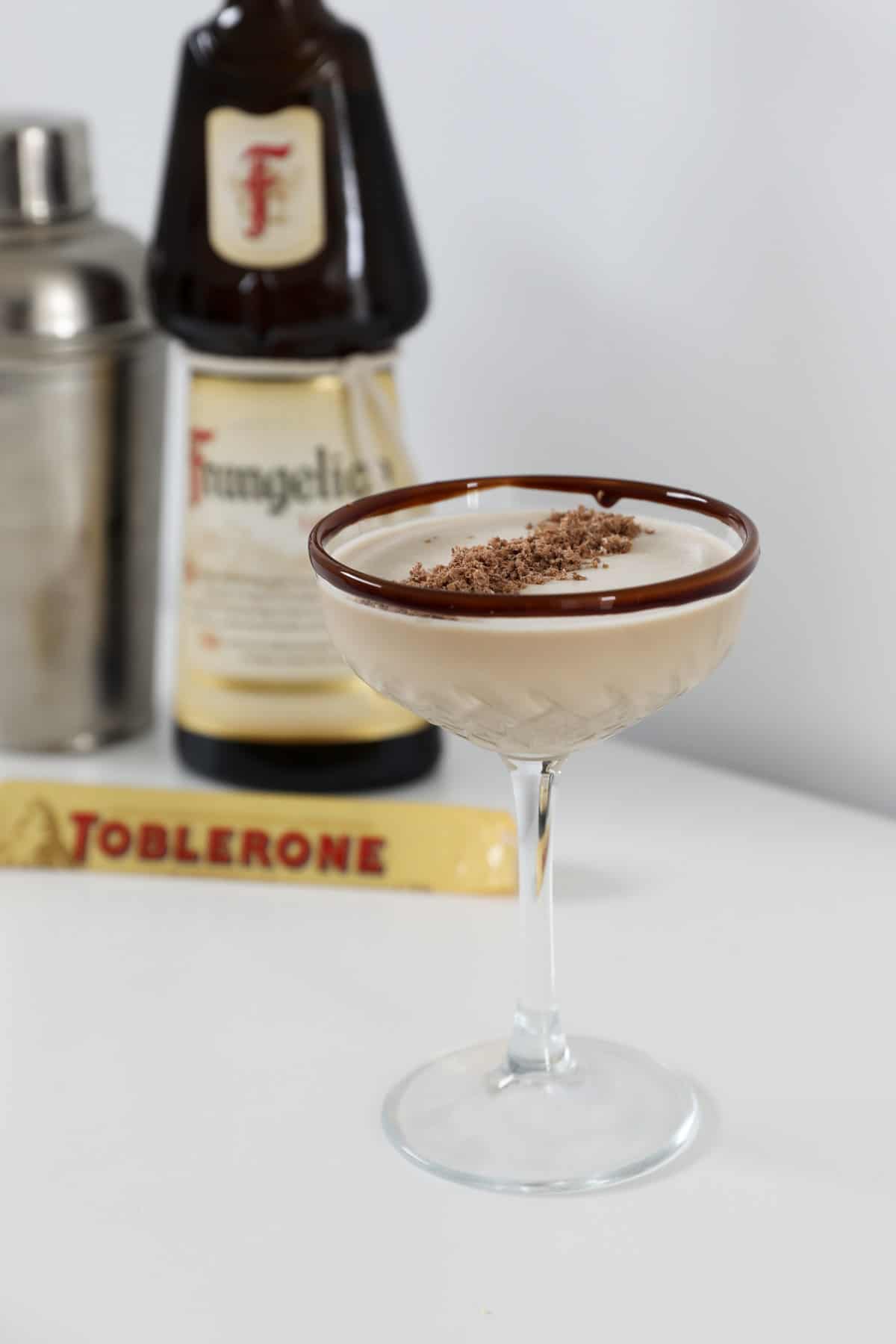 A Toblerone cocktail in a cocktail glass, in front of a bottle of Frangelico and a Toblerone bar.