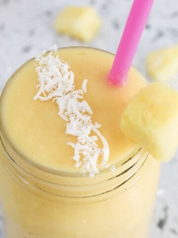 An overhead shot of a yellow mango and pineapple smoothie with coconut on top.