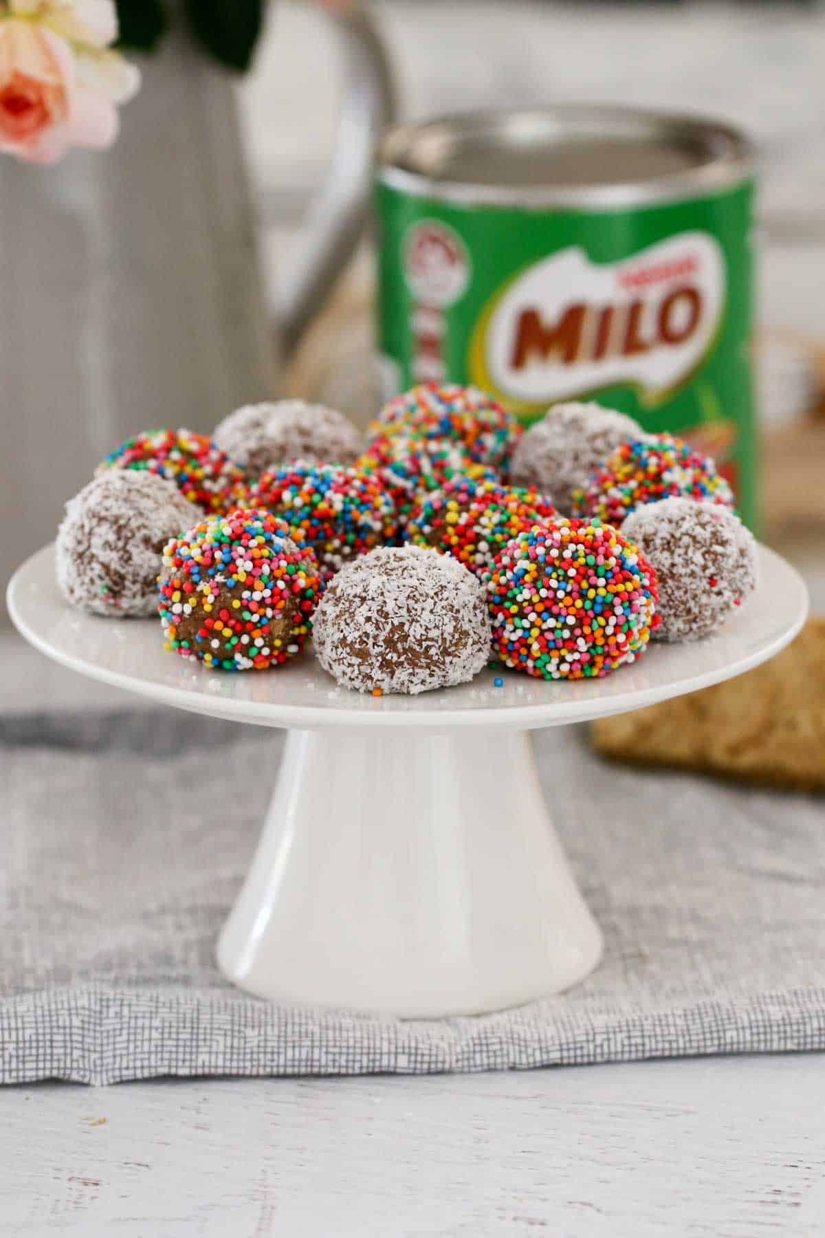 A plate of colourful balls on a white cake stand, with a tin of Milo in the background.