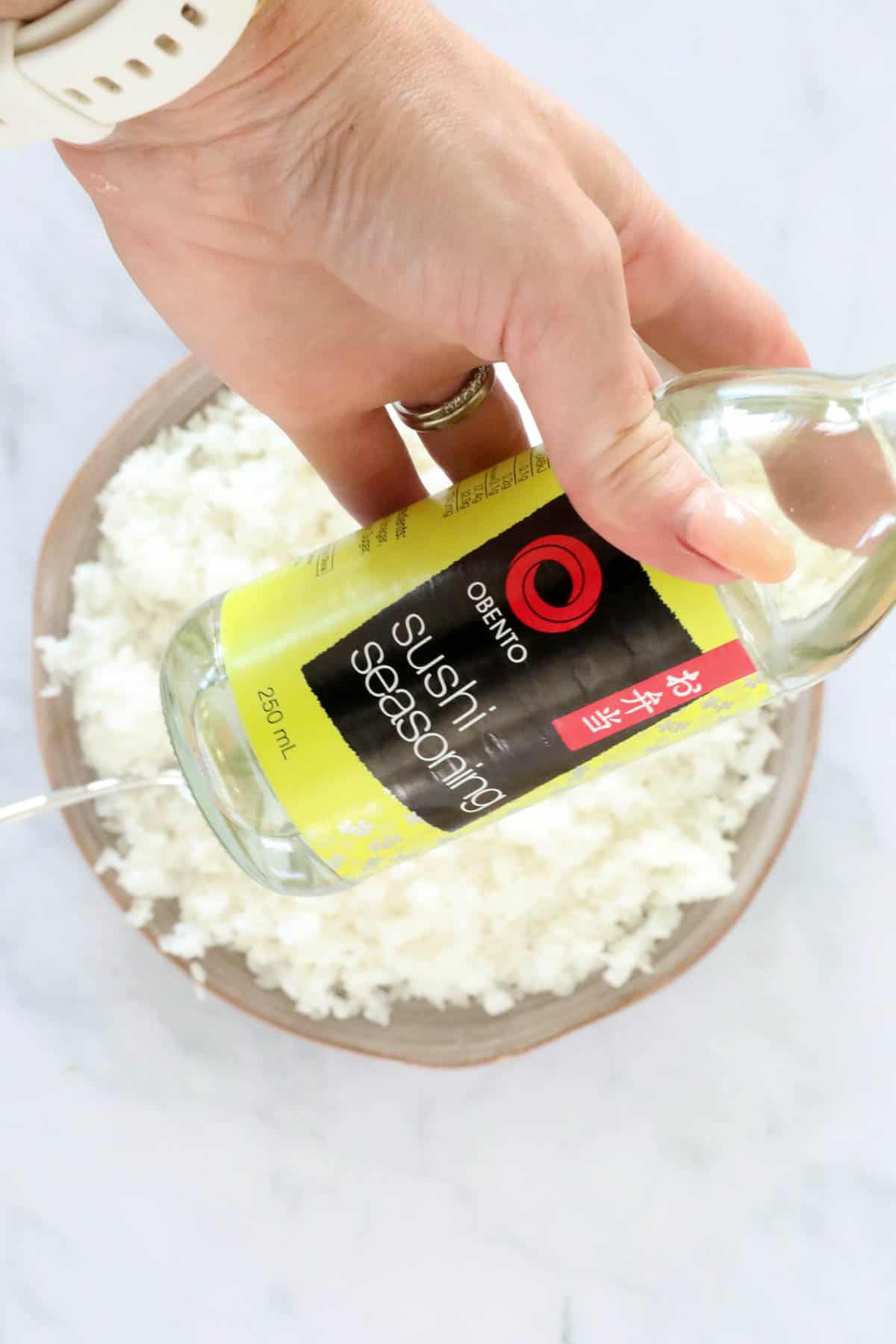 A bottle of sushi seasoningheld over a bowl of rice.