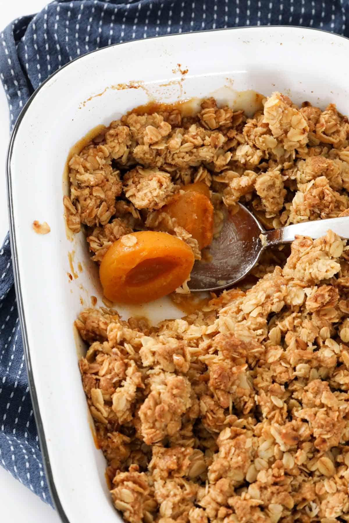 A dish of oat crumble with a portion removed and a spoon in the dish.