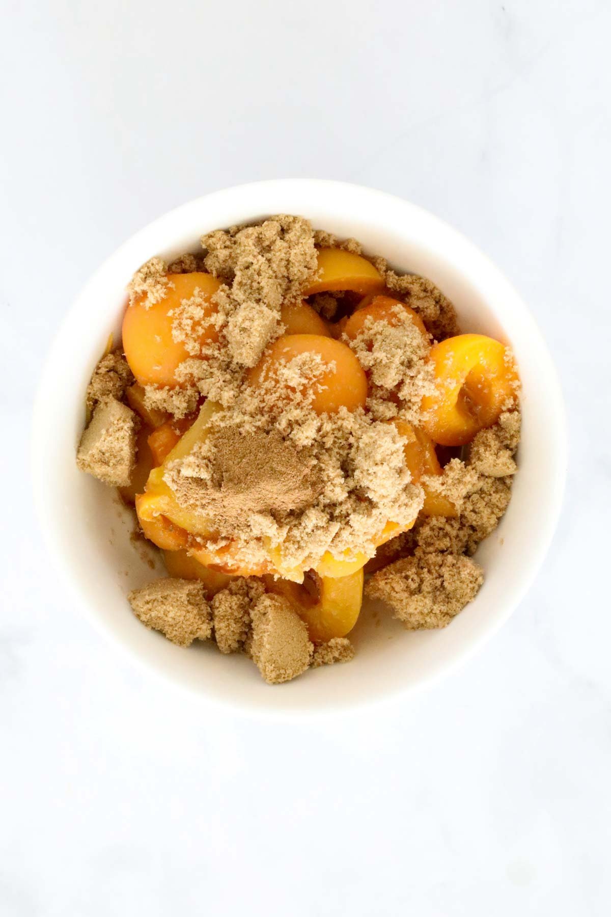 A white bowl filled with apricots, brown sugar and ground cinnamon.