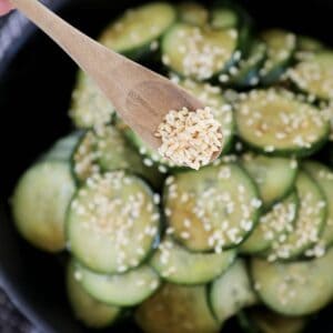 Sesame seeds being poured onto a sweet and soy Asian cucumber salad.