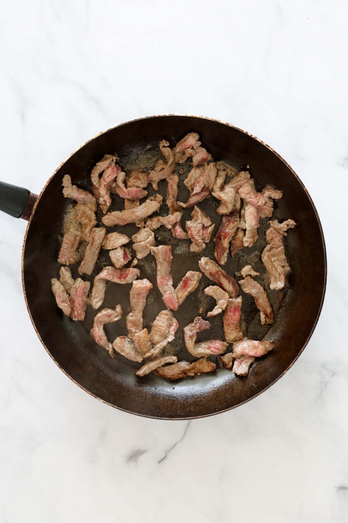 Strips of steak sauteing in a frying pan.