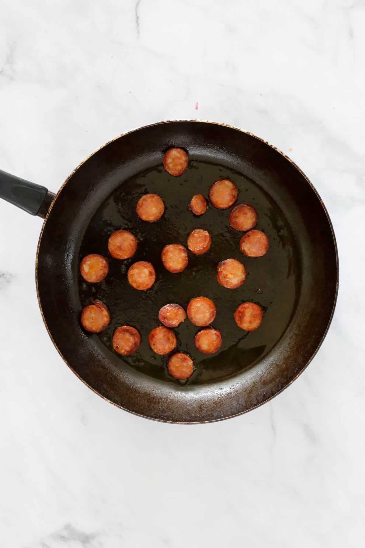 Slices of chorizo fried in a frying pan.