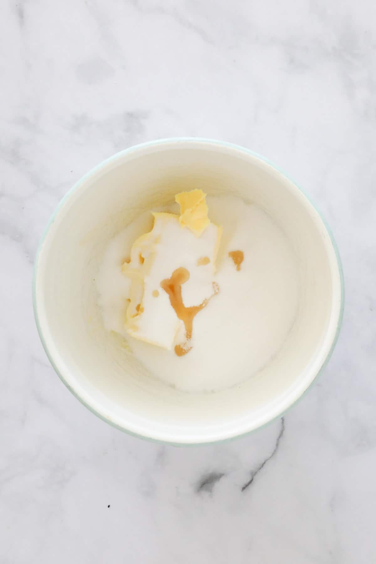 Butter, sugar and vanilla essence in a white bowl.