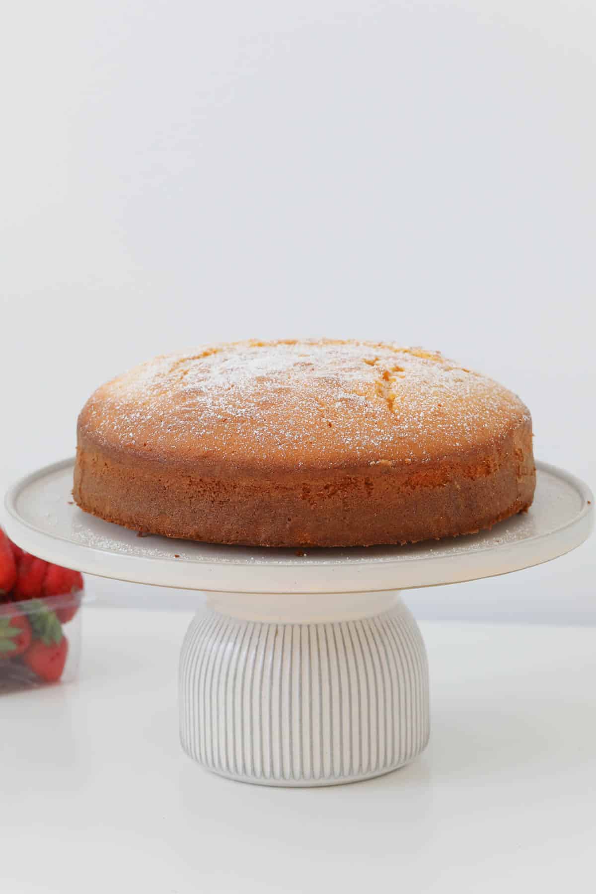 A butter cake dusted with icing sugar, served on a white cake stand.