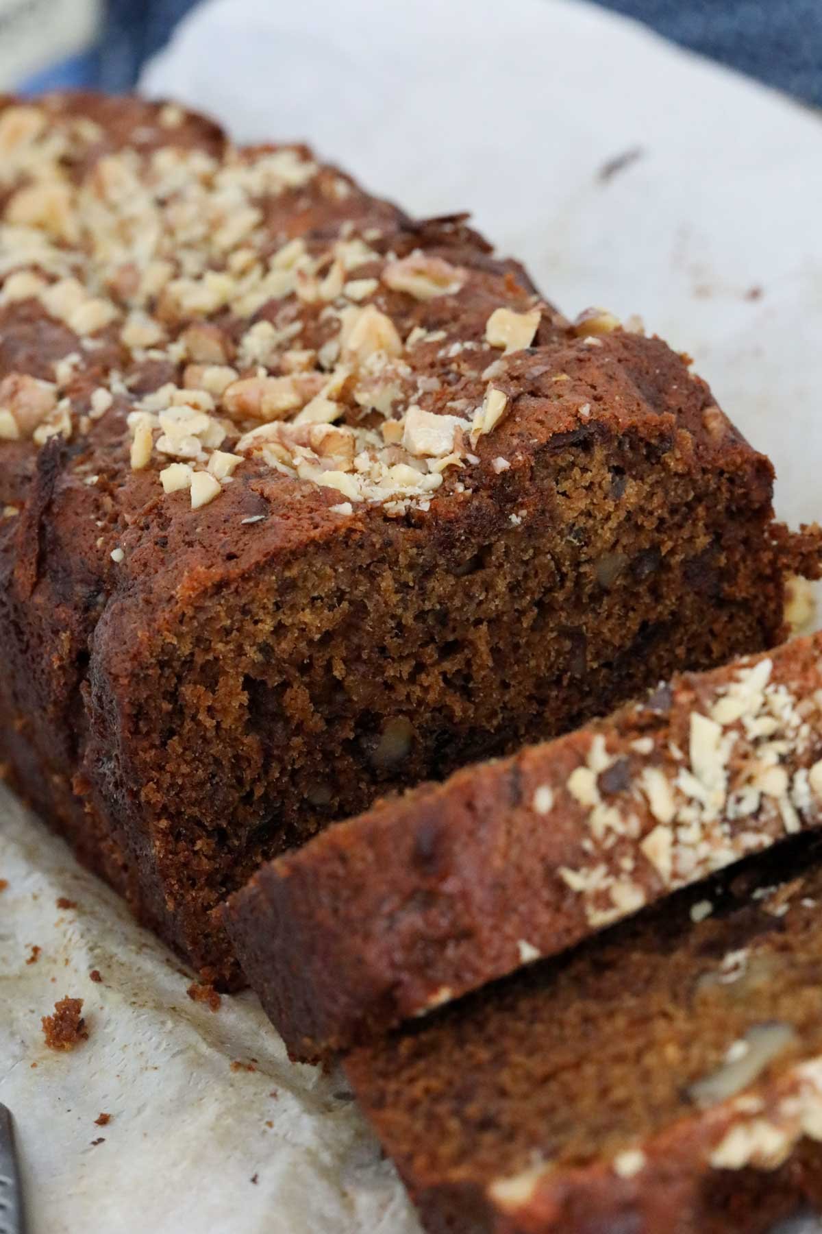 A close up of a loaf sprinkled with chopped walnuts, with a slice cut.