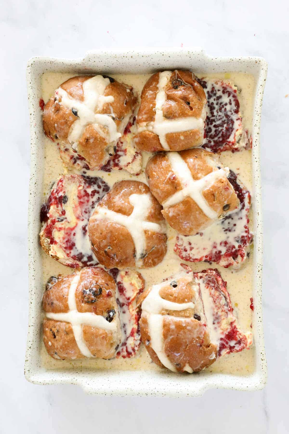 Egg custard poured over hot cross buns in a baking dish.