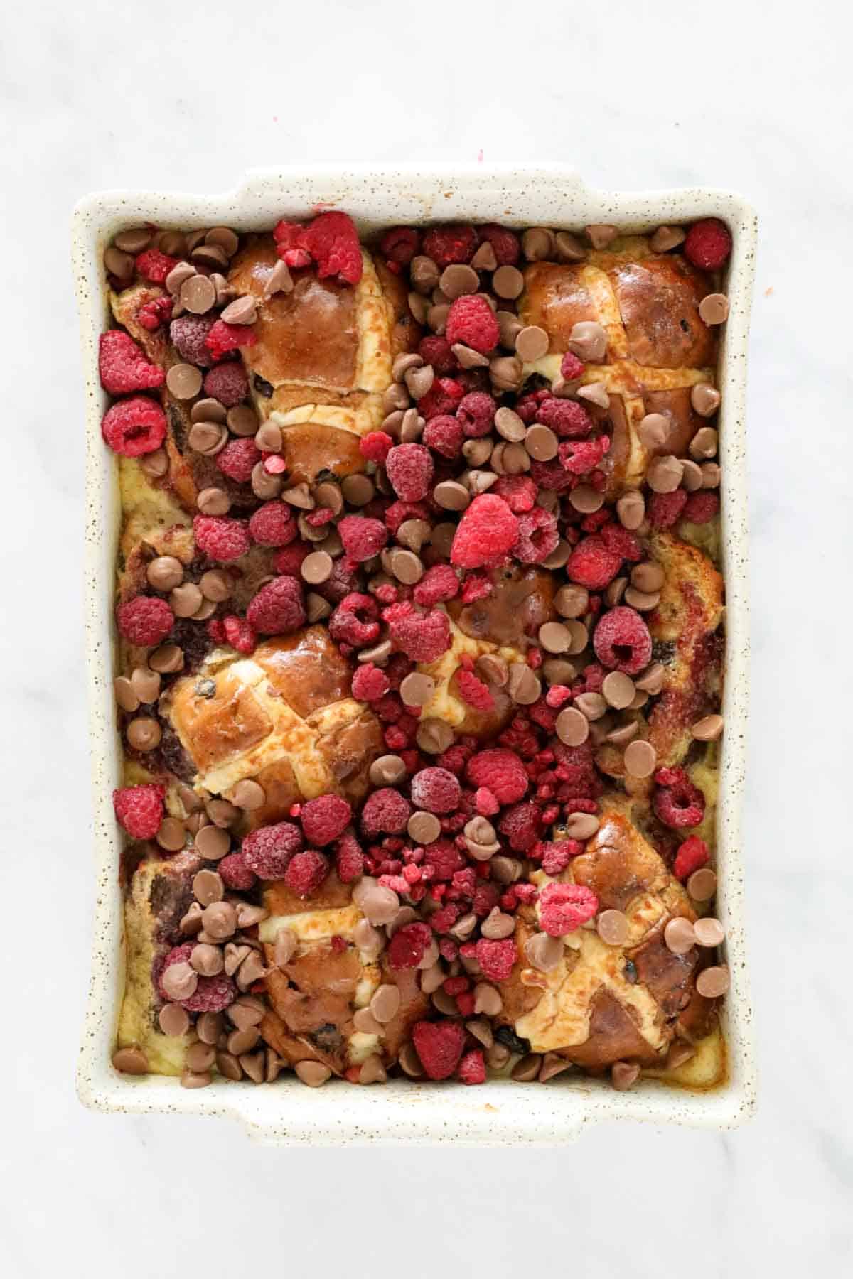 Raspberries and chocolate chips on top of hot cross buns in a baking dish.